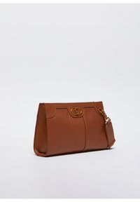 Borsa a mano in pelle marrone con un design strutturato, dotata di accessori in oro, un accento del logo e una tracolla removibile. Tessuto liscio e base piatta.