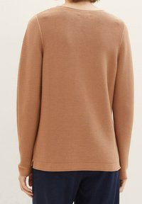 Pull en maille marron avec une texture côtelée, doté d'un col rond et de détails fendus sur les côtés, conçu pour une coupe décontractée.
