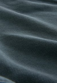 Textilstoff in einem mitteldunklen Blau mit einer strukturierten Webart, die sanfte Falten und eine wellenförmige Oberfläche zeigt.