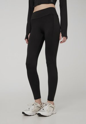 Leggings sportivi neri con vita alta, caratterizzati da una superficie liscia e cuciture laterali sottili, abbinati a sneakers leggere.