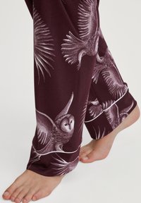 Bordeaux-kleurige pyjamabroek met een witte uilenprint, voorzien van een zachte textuur en een relaxte pasvorm. Het ontwerp bevat gedetailleerde illustraties van uilen en verenpatronen.
