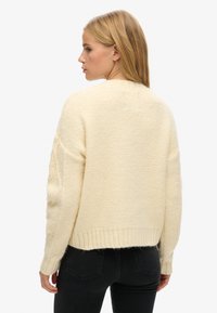 Sweter w kolorze kremowym, wykonany na drutach, o teksturowanej powierzchni, z prążkowanym dołem i nieco oversize'owym krojem. Posiada długie rękawy i okrągły dekolt.