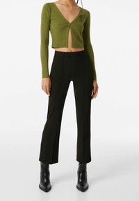 Olivgrön ribbad croppad cardigan med knäppning, ihop med svarta tajta byxor med sidostripes och ankelhöga klackskor.