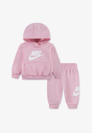 Różowy dres z miękkiego materiału składający się z bluzy z kapturem i spodni dresowych. Bluza ma kieszeń z przodu i biały logo Nike; spodnie wyposażone są w elastyczny pas i mankiety.
