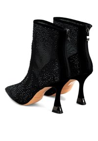 Cizme negre până la gleznă, cu vârfuri ascuțite, țesătură din plasă cu țepușe, fermoare la spate și tocuri subțiri, înalte, cu vârfuri metalice.