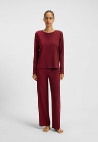 Burgundi loungewear-setti, jossa on pitkähihainen rento paita ja siihen sopivat löysät housut. Pehmeä rakenne, minimalistinen muotoilu.