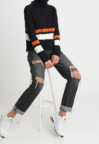 Mörkblå ribbad polotröja med orange och vita ränder, kombinerad med slitna svarta jeans och vita sneakers.