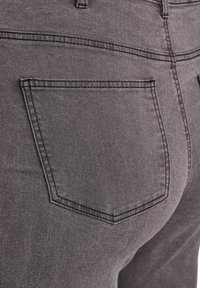Jeans de mezclilla gris con un único bolsillo trasero angular y costuras visibles. La tela tiene una textura suave y un ligero estiramiento.