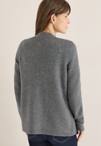 Šedý žebrovaný pletený svetr s dlouhými rukávy a kulatým výstřihem. Tkanina působí měkce, má texturovaný povrch a volný střih.