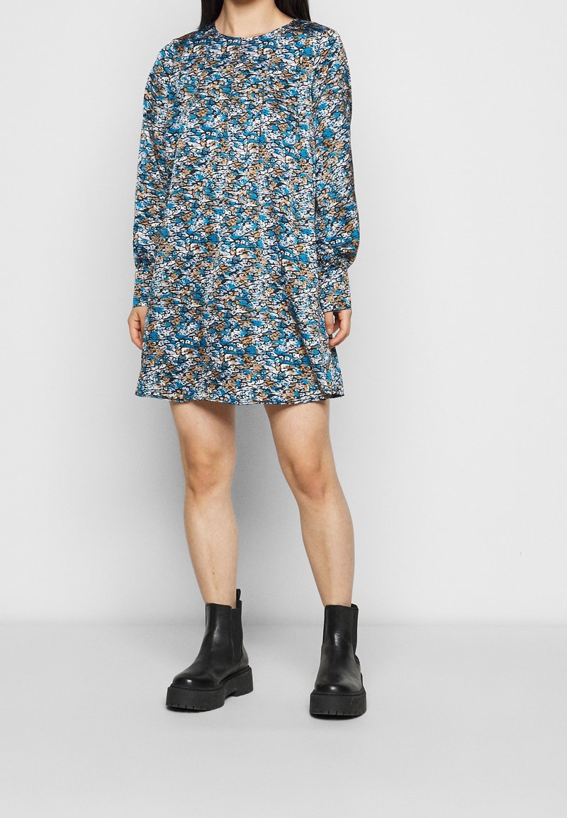 Květinové dlouhé šaty s dlouhým rukávem v modré, hnědé a bílé barvě; volný střih s kulatým výstřihem. Nosené s černými chunky kotníkovými botami.