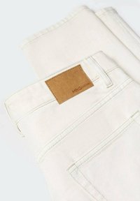 Jean en denim écru plié avec une poche arrière visible et un patch en cuir rectangulaire marron marqué "MNG DENIM".