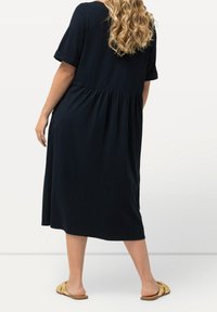 Tummansininen midi-mekko, jossa on lyhyet käännetyt hihat, rypytetty vyötärö ja laskostettu hame. Kivuton kangas, jolla on pehmeä rakenne.