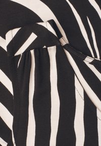 Black and white striped fabric with gathered detailing and visible stitching, forming part of a garment's sleeve or cuff area.