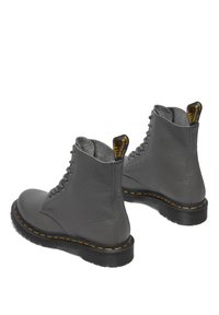 Botas de tobillo de cuero gris con cordones en la parte delantera, acabado texturizado, costuras amarillas en la suela y una pestaña en la parte posterior para facilitar su colocación.