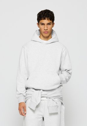 Hoodie gris clair en tissu doux, doté d'une poche kangourou, d'une capuche avec cordon de serrage et de poignets côtelés. Porté avec un pantalon assorti.
