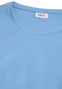Chemise bleu clair à col rond avec une étiquette blanche visible cousue à l'intérieur du col portant l'inscription "CECIL".