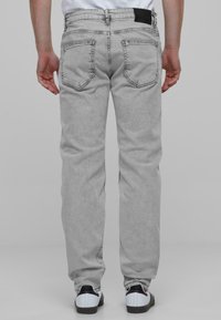 Hallid hallid teksad, lõdva lõikega, klassikaliste tagataskutega ja musta sildiga vööpaelal. Seljas valged ja mustad spordijalatsid.