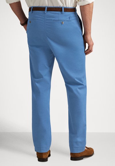 Calças azul-claro feitas de tecido com textura suave; apresentam dois bolsos traseiros com botões dourados e um cinto de couro castanho.