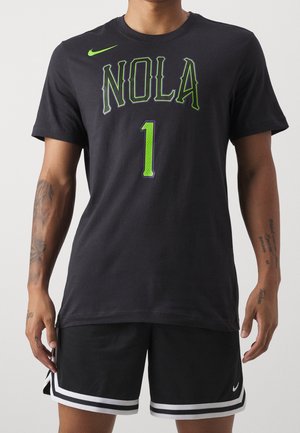 Man wearing black Nike shorts and black t-shirt with green "NOLA" text and number 1 on front, arms visible with tattoos.