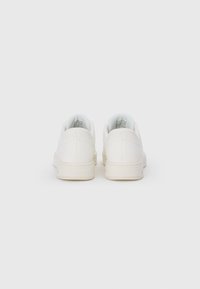 White sneakers with a smooth leather upper, round toe, padded collar, and subtle perforations at the heel. Flat rubber sole.