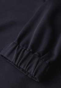 Tummansininen kangas, jossa on kootut elastiset hihansuut pitkissä hihoissa, näyttäen tekstiiliä ja ompelujälkeä.