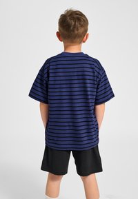 Blauw gestreept T-shirt met korte mouwen, voorzien van zwarte horizontale strepen. Draagt bij zwarte korte broek. De stof lijkt zacht en casual.