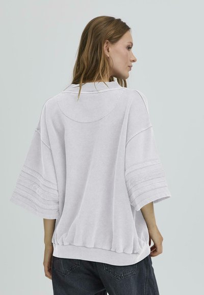 Sweatshirt alb de mari dimensiuni, cu umeri lăsați, guler cu nervuri și dungi texturate pe mâneci. Tivul strâns adaugă formă.