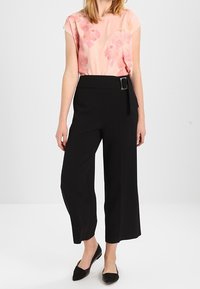 Blouse florale pêche à manches courtes et coupe ample, associée à un pantalon noir taille haute à jambe large avec une ceinture et une boucle.