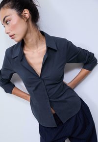 Dark gray button-up shirt with a collar, long sleeves, and a tailored fit. Smooth texture, showing subtle contours on fabric.