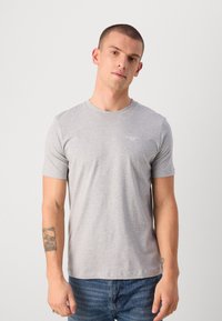 Tricou din bumbac gri, cu mâneci scurte, decolteu rotund și detaliu subtil cu logo pe piept. Purtați cu blugi din denim albaștri.