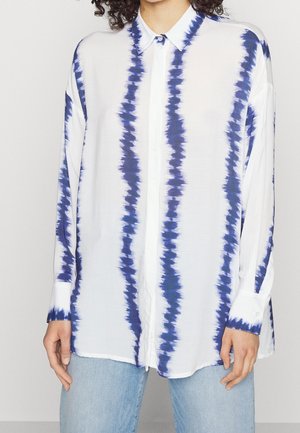 Chemise blanche avec des rayures tie-dye bleues, manches longues, col boutonné et poignets ; fabriquée en tissu léger, avec une coupe décontractée.