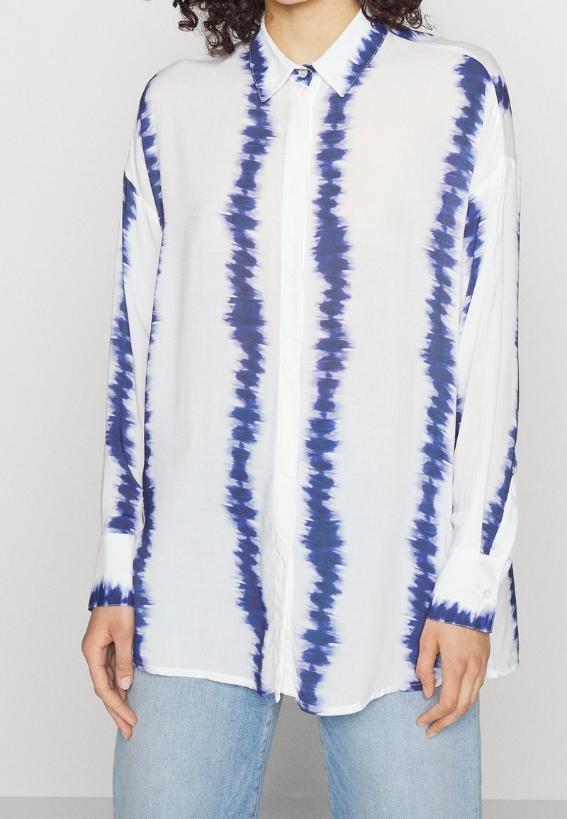 Camicia bianca con righe di tie-dye blu, maniche lunghe, colletto all'italiana e polsini; realizzata in tessuto leggero, presenta una vestibilità morbida.
