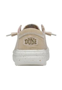 Sneaker in tela beige con esterno testurizzato, dotato di una suola bianca maculata e del logo "Hey Dude". Include linguette in tessuto sul retro.
