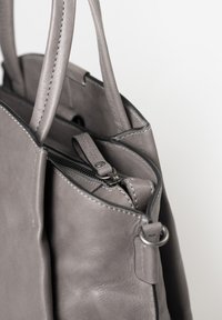Grijze leren totebag met dubbele handvatten, ritssluiting en contrasterende stiksels. Kenmerkt zich door een gladde textuur en een minimalistisch ontwerp.