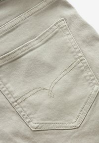 Tejido de mezclilla beige claro con un primer plano de un bolsillo trasero que presenta costuras dobles y un sutil diseño de costura curva.