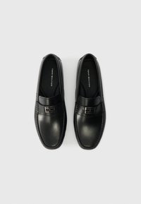 Musta nahkakengät ilman nauhoja, joissa on sileä pinta, koristeellinen nauha metallikomponentilla ja ommeltu yksityiskohta pohjan ympärillä.