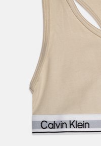 Beige bomulls-bh med racerback-design, med et svart og grått elastisk bånd med "Calvin Klein"-logo nederst.