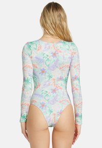 Maillot de bain une pièce à manches longues, en tissu extensible. Présente un motif floral tropical pastel en vert, rose et violet.