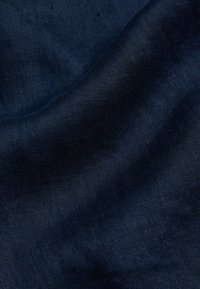 Tessuto di lino blu scuro con trama a vista e pieghe morbide che creano ombre e luci delicate.