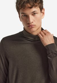Dunkelbrauner Rollkragenpullover aus weichem Stoff, mit einem enganliegenden Kragen und gerippten Bündchen. Glatte Textur mit minimalen Details.