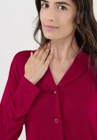 Top de manga larga en magenta profundo con cuello, botones al frente y textura suave. Presenta un corte holgado y un brillo sutil.