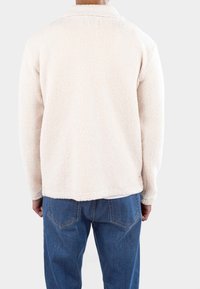 Fleecejacke in Off-White mit strukturierter Oberfläche, mit Kragen und geradem Saum, kombiniert mit blauen Jeans.