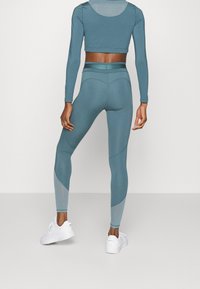 Teal träningsset bestående av en cropped långärmad tröja och högmidjade leggings med meshdetaljer. Slät, elastisk tyg med en figurnära design.
