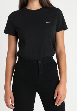 Mustat puuvillapaidat, joissa on lyhyet hihat, pyöreä pääntie ja pieni värikäs logo rinnassa. Yhdistetty korkeavyötäröisiin mustiin farkkuihin.