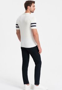 Vit kortärmad pikétröja med marinblå ränder på ärmarna, ribbad krage och nederkant. Matchad med mörka byxor och vita skor.