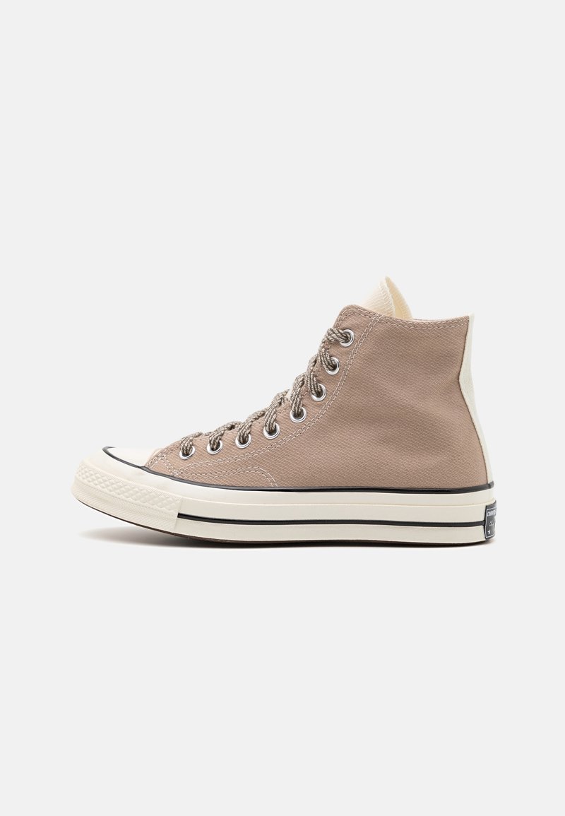 Basket montante en toile marron clair avec semelle en caoutchouc blanche, renfort au bout et détail de bande noire, vue de côté sur fond blanc.