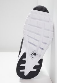 Mustan ja valkoisen urheilusneekerin pohja, jossa on teksturoitu kumipinta, logotieto ja voimakas ilmanvaimennus, sekä erottuva kulutuspinta.