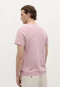 Lyserød bomulds T-shirt med korte ærmer, rund hals og en afslappet pasform. Har en subtil tekstur og et lille mærke i siden.