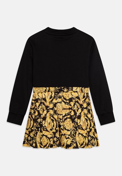 Top negro de manga larga con un patrón floral en amarillo y negro en la mitad inferior, con pliegues y un escote redondo.