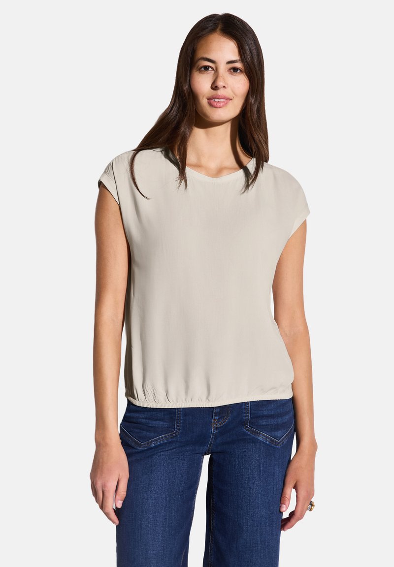 Blusa beige a maniche corte con scollatura tonda e orlo elastico, abbinata a jeans blu con un design classico a cinque tasche.